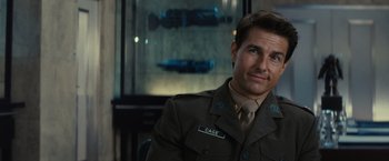 Movie still from “Edge of Tomorrow” (2014), directed by Doug Liman – A man in a military uniform sitting in front of a wall; Close Up shot, Over the shoulder angle