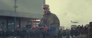 Movie still from “Edge of Tomorrow” (2014), directed by Doug Liman – A man in a military uniform is holding a boot; Medium shot, Low angle