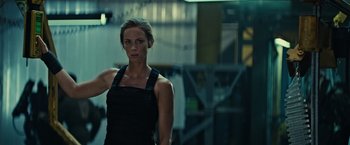 Movie still from “Edge of Tomorrow” (2014), directed by Doug Liman – A woman in a black outfit standing in front of a building; Medium shot, Low angle