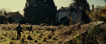 Movie still from “Edge of Tomorrow” (2014), directed by Doug Liman – A person standing in a grassy field near a house; Extreme Wide shot, Low angle