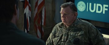 Movie still from “Edge of Tomorrow” (2014), directed by Doug Liman – An older man in a military fatigues looks at the camera; Close Up shot, Over the shoulder angle