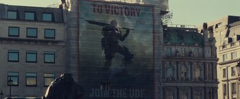 Movie still from “Edge of Tomorrow” (2014), directed by Doug Liman – A poster of a man holding a sword in a city; Wide shot, Low angle