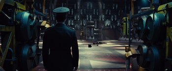 Movie still from “Edge of Tomorrow” (2014), directed by Doug Liman – A man in a military uniform standing in front of a wall; Wide shot, High angle