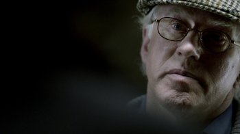 Movie still from “Sherlock” (2010), created by Steven Moffat – An older man wearing glasses and a hat; Close Up shot, Over the shoulder angle