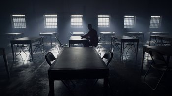Movie still from “Sherlock” (2010), created by Steven Moffat – A man sitting at a table in a room with chairs; Wide shot, High angle