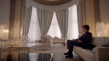 Movie still from “Sherlock” (2010), created by Steven Moffat – A man sitting on top of a couch in a living room; Wide shot, Low angle