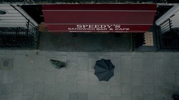 Movie still from “Sherlock” (2010), created by Steven Moffat – A person standing on the sidewalk with an open umbrella; Extreme Wide shot, Overhead angle