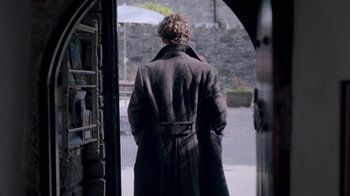 Movie still from “Sherlock” (2010), created by Steven Moffat – A man wearing a long coat walking down a street; Wide shot, Over the shoulder angle