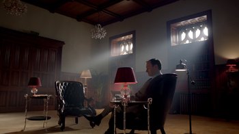 Movie still from “Sherlock” (2010), created by Steven Moffat – A man sitting in a chair in front of a lamp; Wide shot, Low angle