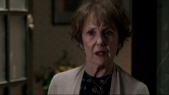 Movie still from “Sherlock” (2010), created by Steven Moffat – An older woman with short brown hair wearing a black shirt; Close Up shot, Over the shoulder angle