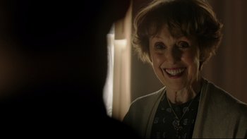 Movie still from “Sherlock” (2010), created by Steven Moffat – An older woman smiling for the camera in the dark; Close Up shot, Over the shoulder angle