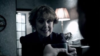 Movie still from “Sherlock” (2010), created by Steven Moffat – A woman sitting at a table holding a cell phone; Close Up shot, Over the shoulder angle