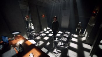 Movie still from “Sherlock” (2010), created by Steven Moffat – A person standing in a room with chairs and a table; Wide shot, High angle