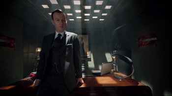 Movie still from “Sherlock” (2010), created by Steven Moffat – A man in a suit standing in front of a desk; Medium shot, Low angle