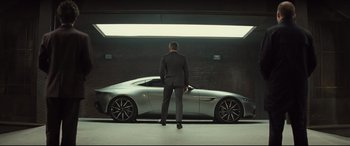 Movie still from “Spectre” (2015), directed by Sam Mendes – A man in a suit standing in front of a silver car; Wide shot, Low angle
