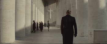 Movie still from “Spectre” (2015), directed by Sam Mendes – A group of people standing in a building with a cross on the wall; Wide shot, Low angle