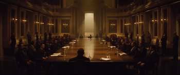 Movie still from “Spectre” (2015), directed by Sam Mendes – A group of people sitting around a long wooden table; Wide shot, High angle