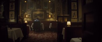 Movie still from “Spectre” (2015), directed by Sam Mendes – A man sitting in a chair in a restaurant; Wide shot, Over the shoulder angle