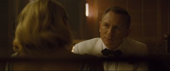 Movie still from “Spectre” (2015), directed by Sam Mendes – A man in a white suit sitting in front of a woman; Close Up shot, Over the shoulder angle