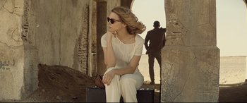 Movie still from “Spectre” (2015), directed by Sam Mendes – A woman sitting on top of a suitcase in front of a man; Medium shot, Low angle