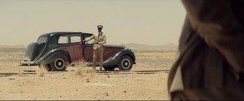 Movie still from “Spectre” (2015), directed by Sam Mendes – A man standing next to an old car in the desert; Wide shot, Over the shoulder angle