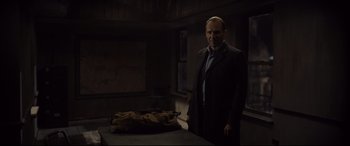 Movie still from “Spectre” (2015), directed by Sam Mendes – A man standing next to a bag in a dark room; Medium shot, Over the shoulder angle