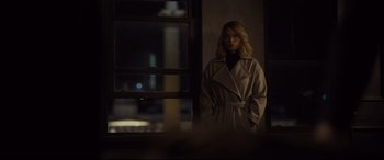 Movie still from “Spectre” (2015), directed by Sam Mendes – A woman in a trench coat standing in front of a window at night; Medium shot, Over the shoulder angle