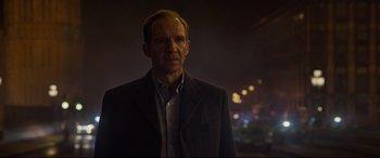 Movie still from “Spectre” (2015), directed by Sam Mendes – A man wearing a suit and tie standing in front of lights; Close Up shot, Over the shoulder angle