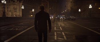 Movie still from “Spectre” (2015), directed by Sam Mendes – A man standing on the side of a road at night; Wide shot, Over the shoulder angle