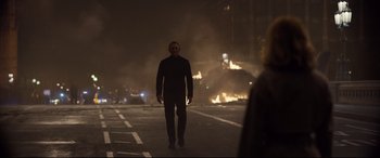 Movie still from “Spectre” (2015), directed by Sam Mendes – A man walking down the street in front of a burning building; Wide shot, Over the shoulder angle