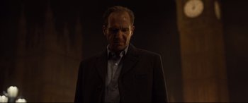 Movie still from “Spectre” (2015), directed by Sam Mendes – A man in a suit and tie standing in a dark room; Close Up shot, Low angle