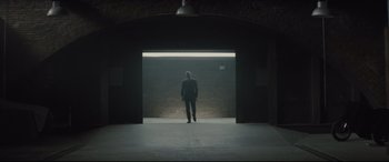 Movie still from “Spectre” (2015), directed by Sam Mendes – A man in a suit is standing in a dark room; Wide shot, Low angle