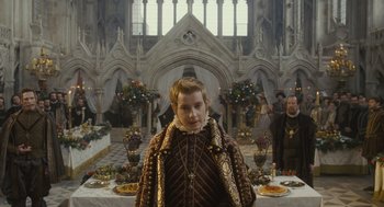 Movie still from “Elizabeth: The Golden Age” (2007), directed by Shekhar Kapur – A man standing in front of a table of food; Medium shot, Over the shoulder angle