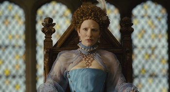Movie still from “Elizabeth: The Golden Age” (2007), directed by Shekhar Kapur – A woman in a blue dress sitting on a wooden chair; Medium shot, Low angle