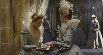 Movie still from “Elizabeth: The Golden Age” (2007), directed by Shekhar Kapur – Two women dressed in period costumes are holding a pan; Medium shot, Over the shoulder angle