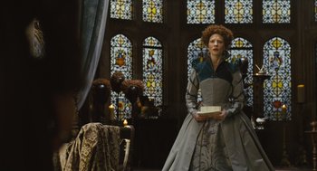 Movie still from “Elizabeth: The Golden Age” (2007), directed by Shekhar Kapur – A woman dressed in medieval clothing stands in front of stained glass windows; Medium shot, Over the shoulder angle