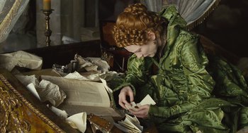 Movie still from “Elizabeth: The Golden Age” (2007), directed by Shekhar Kapur – A woman in a green coat looking at papers; Medium shot, High angle