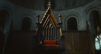 Movie still from “Elizabeth: The Golden Age” (2007), directed by Shekhar Kapur – An ornate wooden chair in a dark room; Extreme Wide shot, Low angle