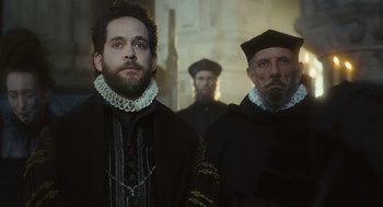 Movie still from “Elizabeth: The Golden Age” (2007), directed by Shekhar Kapur – Two men dressed in medieval clothing standing next to each other; Medium shot, Over the shoulder angle