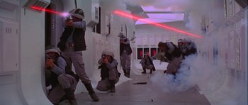 Movie still from “Star Wars: Episode IV - A New Hope” (1977), directed by George Lucas – A group of people in a room with guns and smoke; Wide shot, Low angle