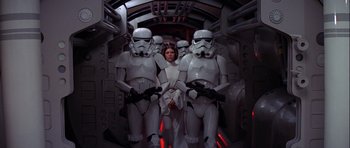 Movie still from “Star Wars: Episode IV - A New Hope” (1977), directed by George Lucas – A woman standing between two white stormtroopers; Wide shot, Low angle