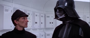 Movie still from “Star Wars: Episode IV - A New Hope” (1977), directed by George Lucas – Two men in suits and hats are looking at each other in a room; Close Up shot, Over the shoulder angle