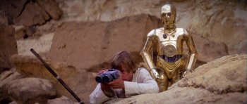 Movie still from “Star Wars: Episode IV - A New Hope” (1977), directed by George Lucas – A young man holding a pair of binoculars next to a star wars character; Medium shot, Over the shoulder angle