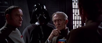 Movie still from “Star Wars: Episode IV - A New Hope” (1977), directed by George Lucas – A man in a suit and tie next to a man in a darth vader mask; Close Up shot, Over the shoulder angle