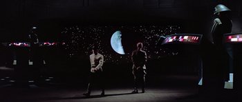 Movie still from “Star Wars: Episode IV - A New Hope” (1977), directed by George Lucas – Two men standing in front of a projection of the moon; Extreme Wide shot, Low angle