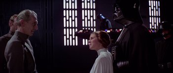 Movie still from “Star Wars: Episode IV - A New Hope” (1977), directed by George Lucas – A woman in a white shirt is standing in front of a wall; Medium shot, Over the shoulder angle