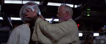 Movie still from “Star Wars: Episode IV - A New Hope” (1977), directed by George Lucas – An older man with a beard is holding something in his mouth; Close Up shot, Over the shoulder angle