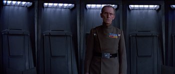 Movie still from “Star Wars: Episode IV - A New Hope” (1977), directed by George Lucas – An old man in a uniform standing in front of a wall; Medium shot, Low angle