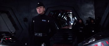 Movie still from “Star Wars: Episode IV - A New Hope” (1977), directed by George Lucas – A man in a black uniform standing in a tunnel; Medium shot, Low angle