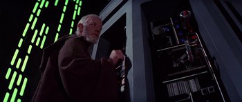 Movie still from “Star Wars: Episode IV - A New Hope” (1977), directed by George Lucas – An older man holding a sword in a dark room; Medium shot, Low angle